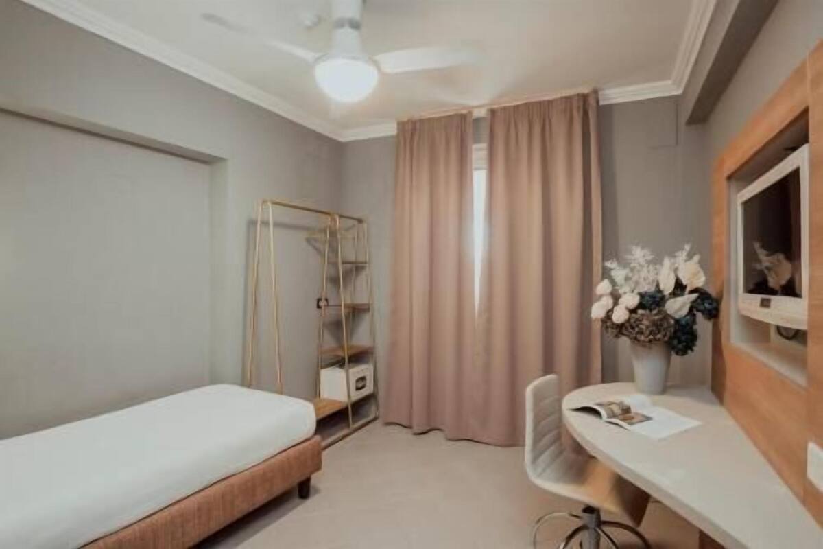 A bedroom with a bed, a desk, a chair, a wardrobe, and a window with curtains.
