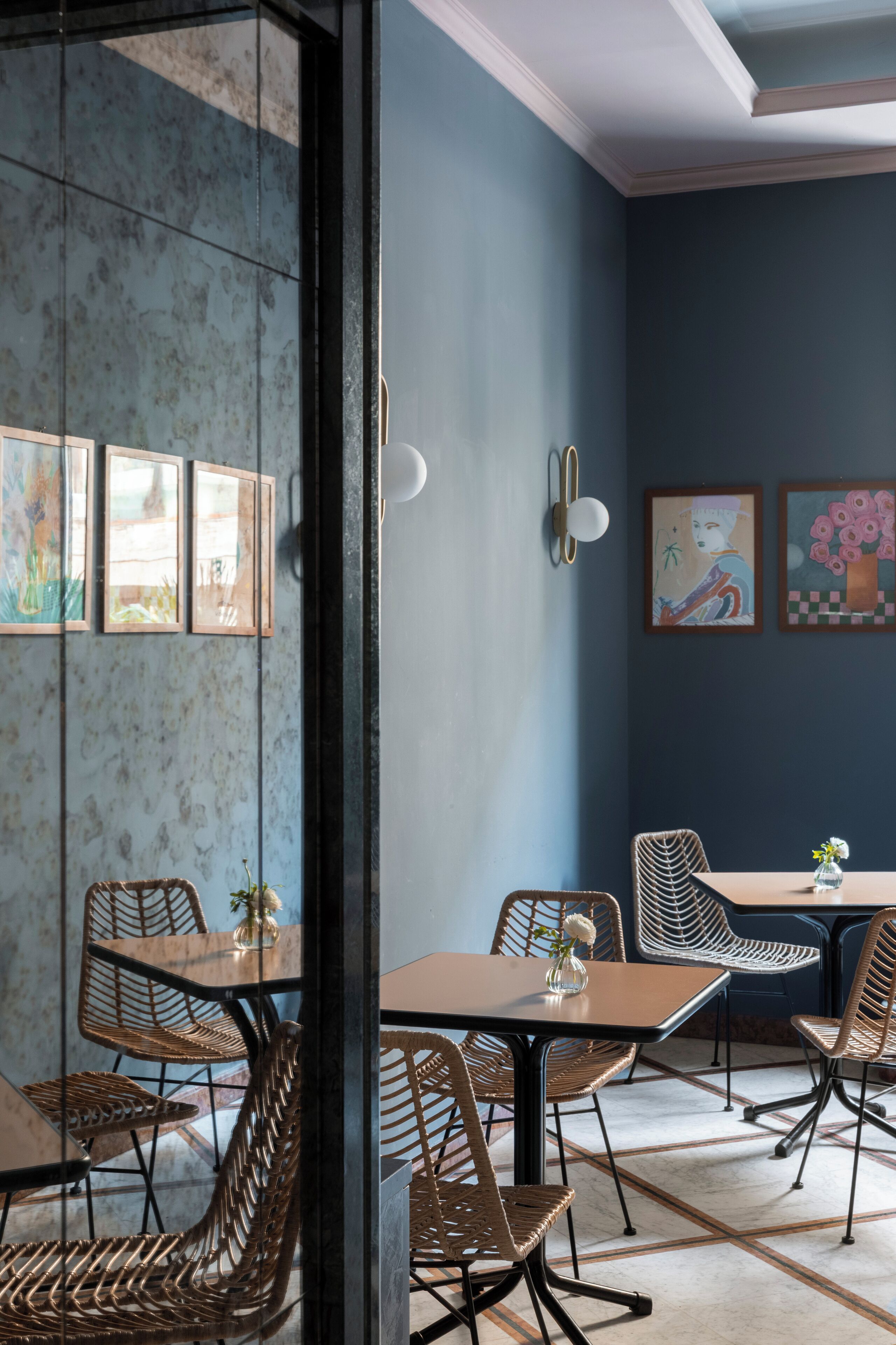 Un espace de salle à manger moderne, avec un mélange de meubles en métal et en osier, un mur d’accent bleu et des œuvres d’art.