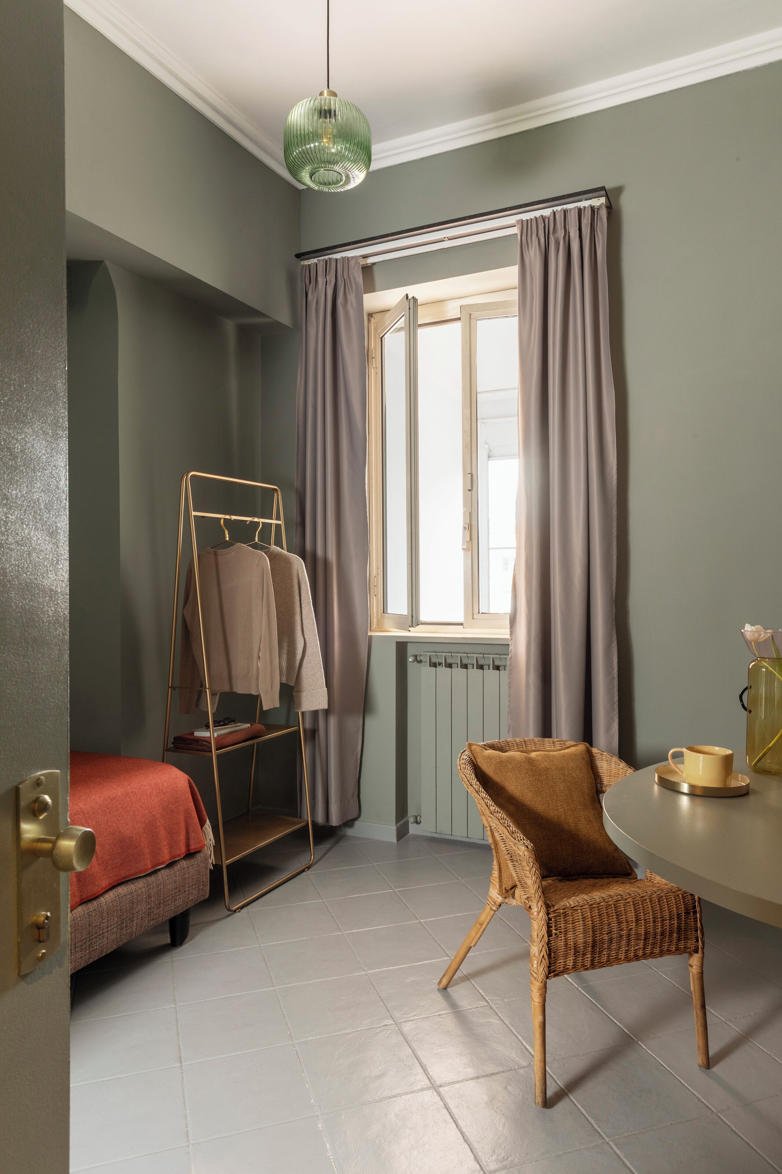 Une pièce comprenant un lit, une chaise, une fenêtre avec des rideaux, un radiateur et un luminaire suspendu.