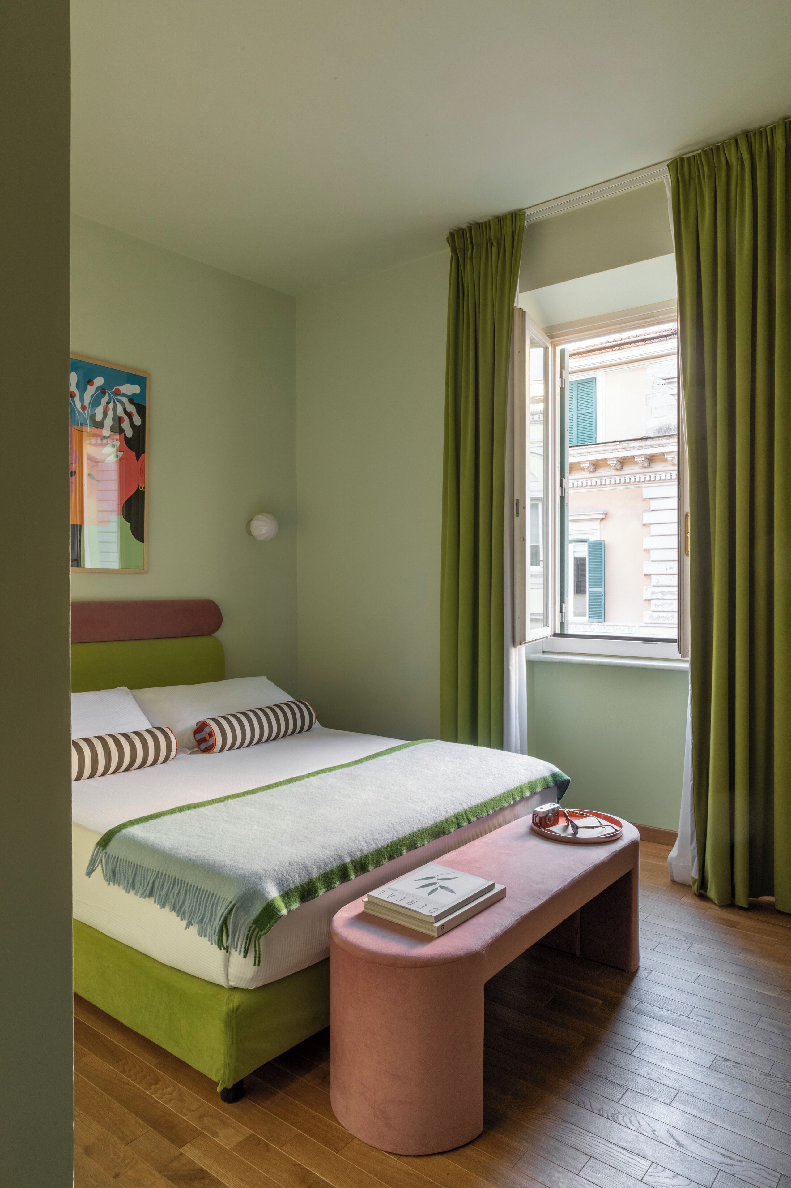A bedroom with a bed, a bench, a window with curtains, and a painting on the wall.