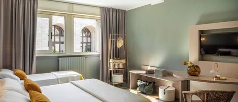 Habitación de hotel con dos camas, un escritorio con televisor, una silla y una ventana con cortinas.