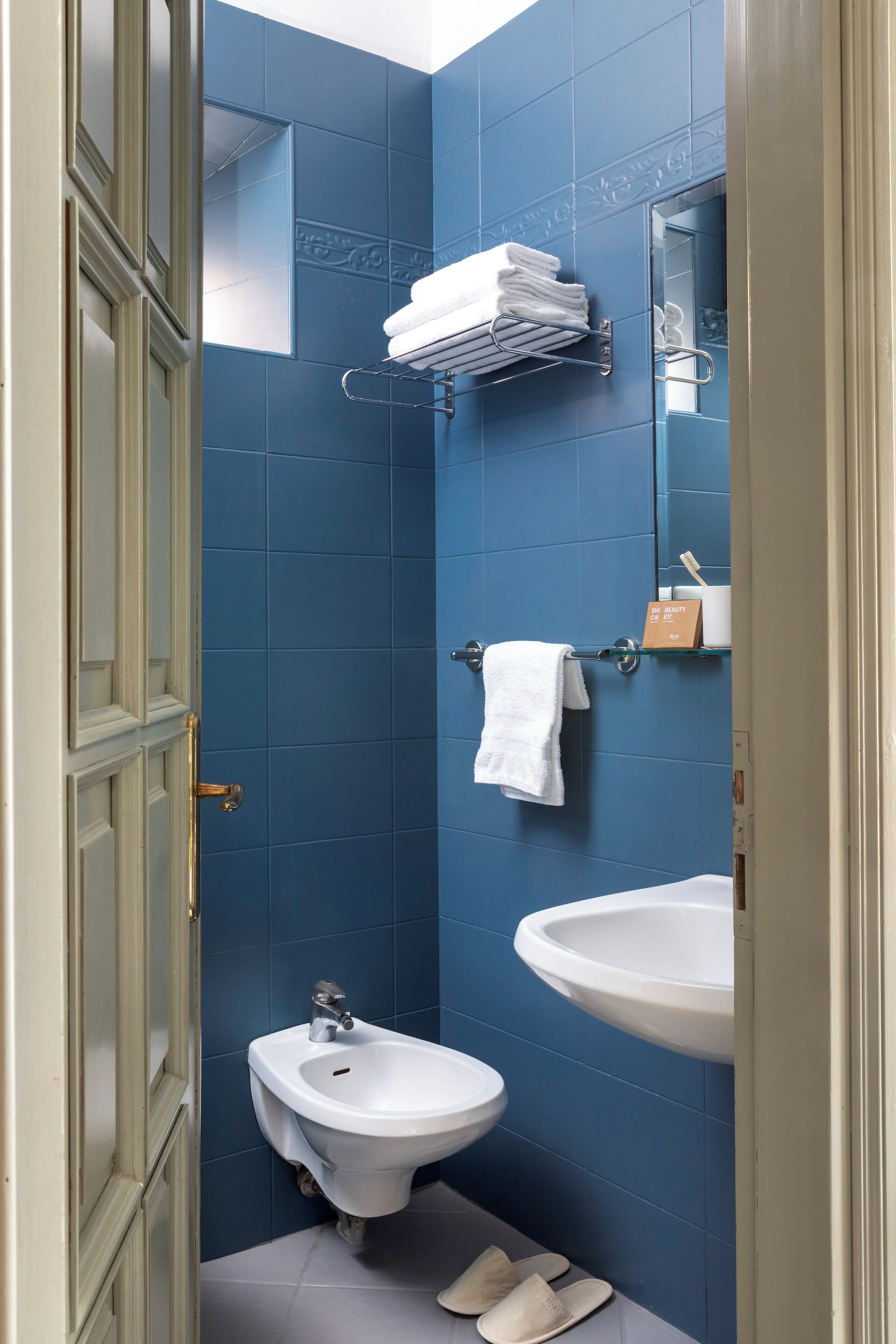A bathroom with blue tiles, a bidet, a sink, and a towel rack.