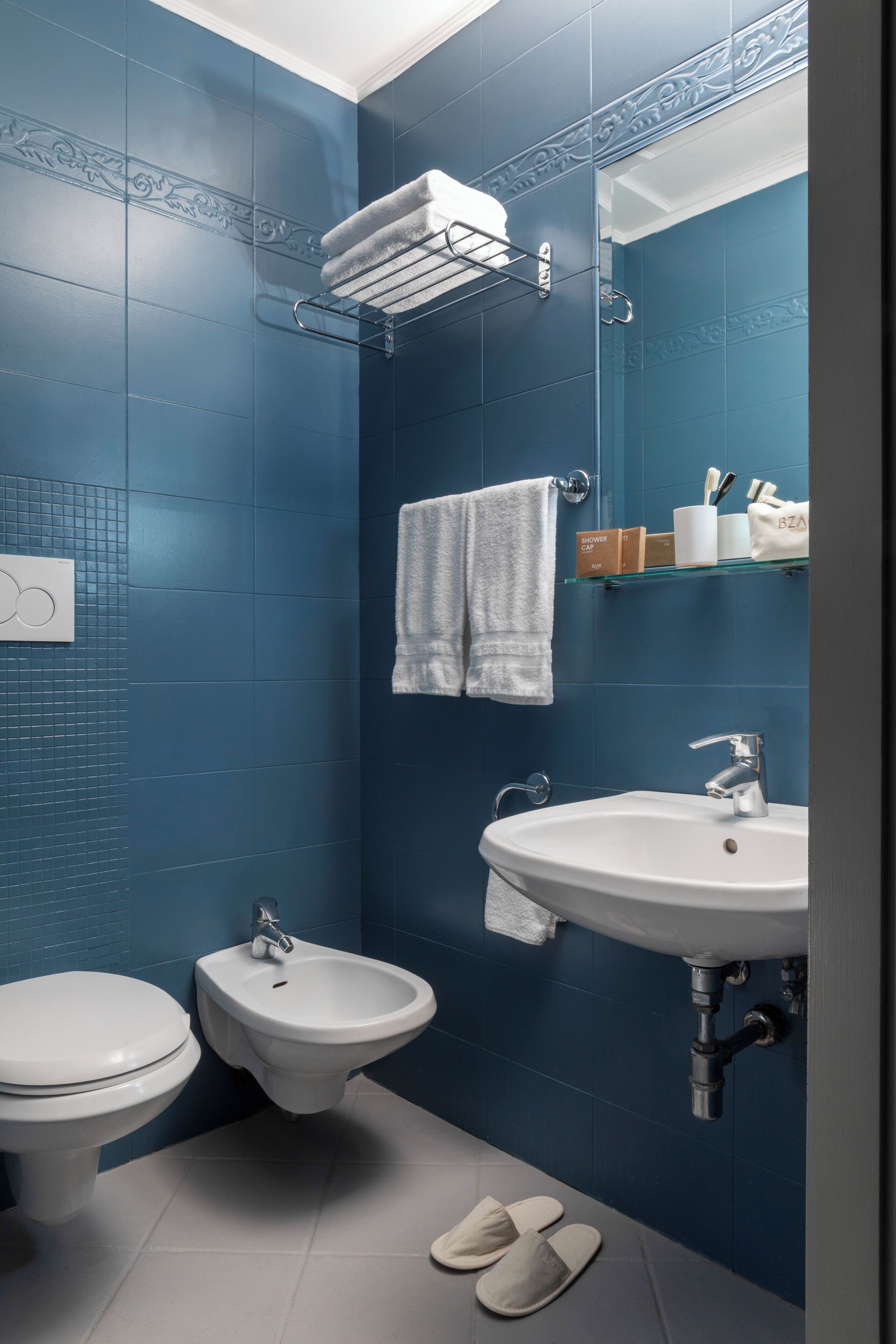 Casa de banho com sanita branca, bidé e lavatório, paredes com azulejos azuis e espelho sobre o lavatório.