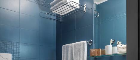 Un baño con inodoro, bidé y lavamanos blancos, paredes con azulejos azules y un espejo sobre el lavamanos.