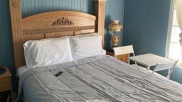 A neatly made bed with a grey quilt, a wooden headboard, and a painting of a beach scene on the wall.