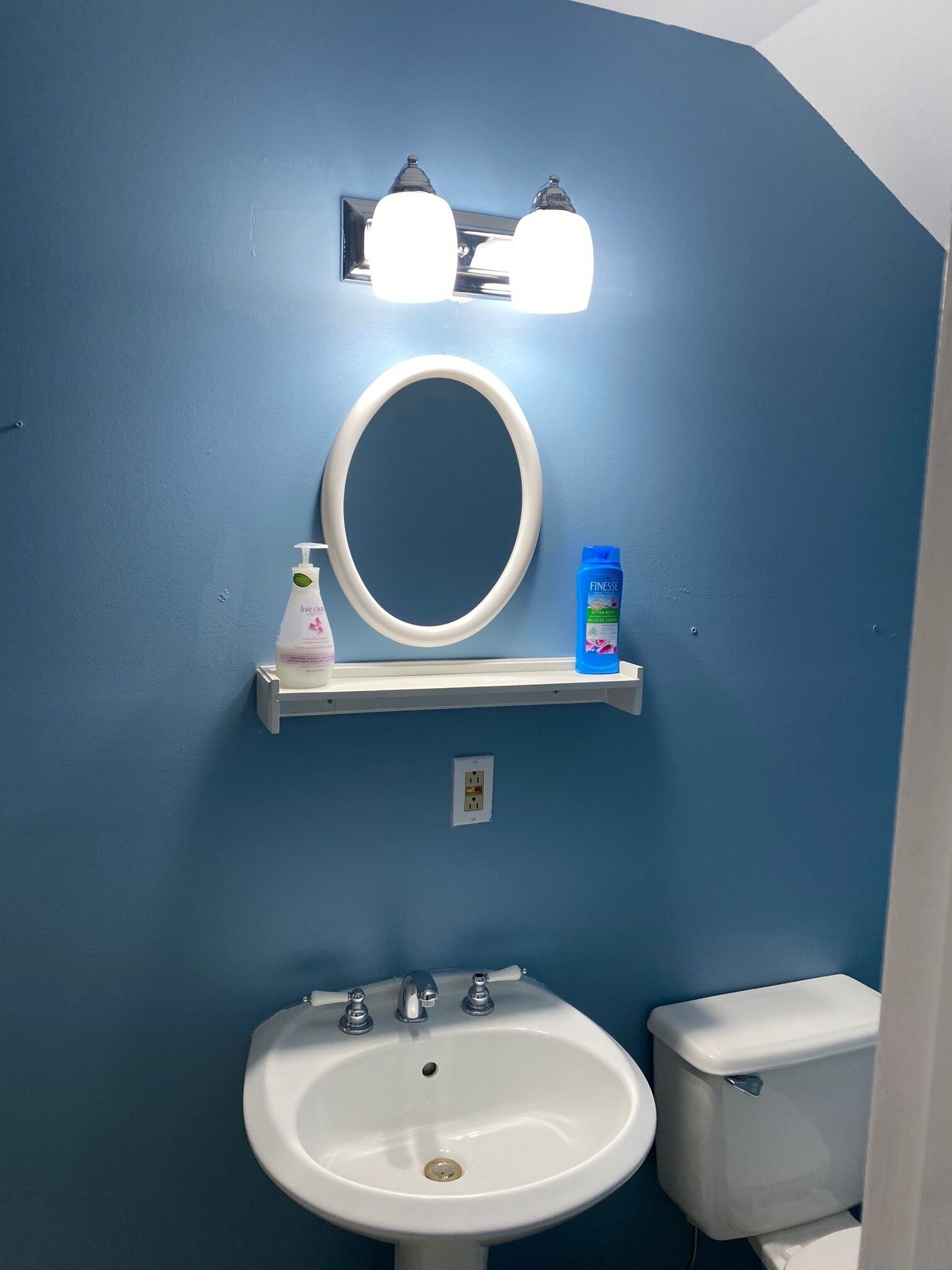 Ein Badezimmer mit blauer Wand, Waschbecken in Weiß, Toilette, Spiegel und Ablage mit Pflegeprodukten.