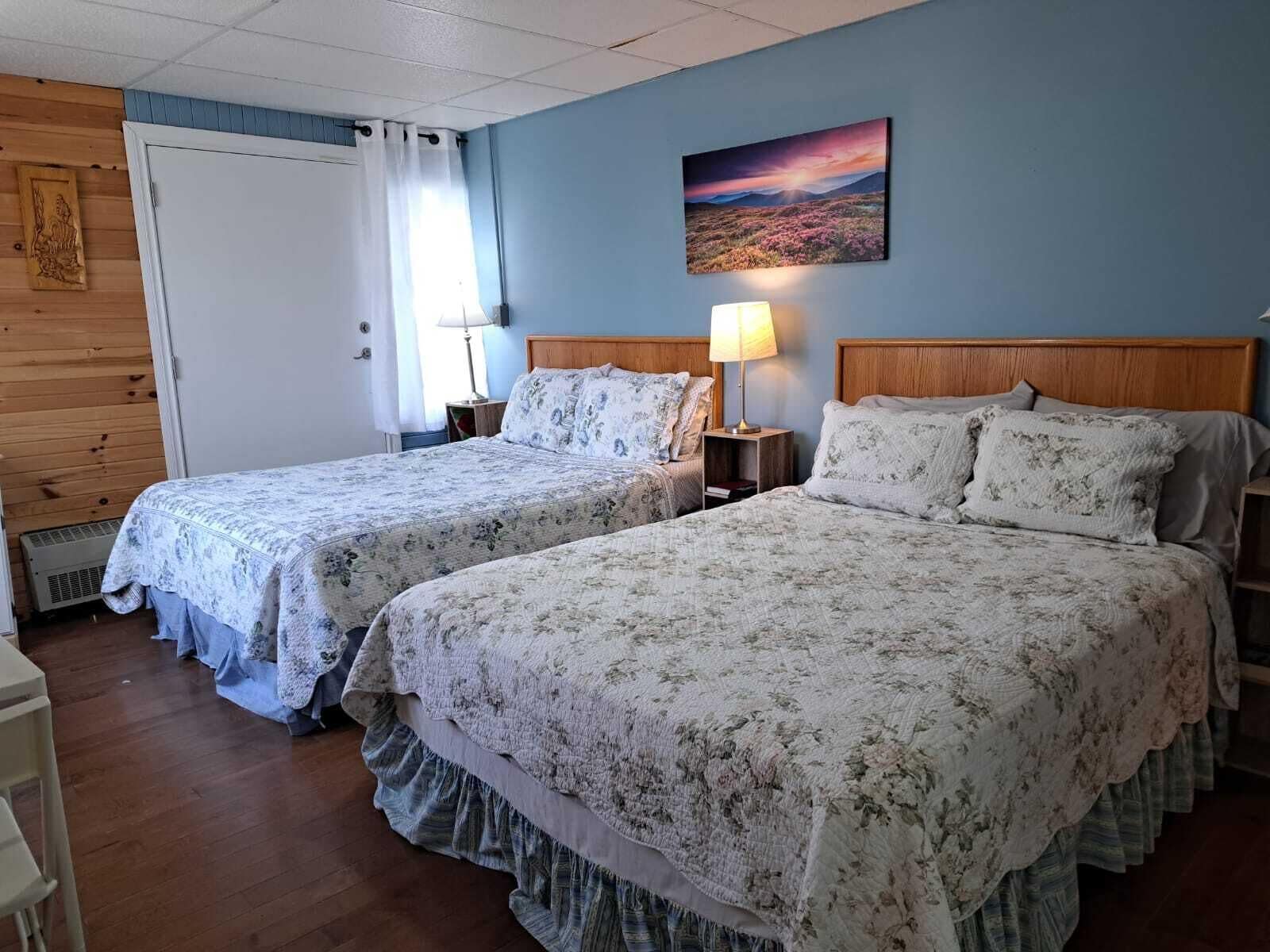 Une chambre avec deux lits, une tête de lit en bois, une table de chevet avec une lampe et un tableau au mur.