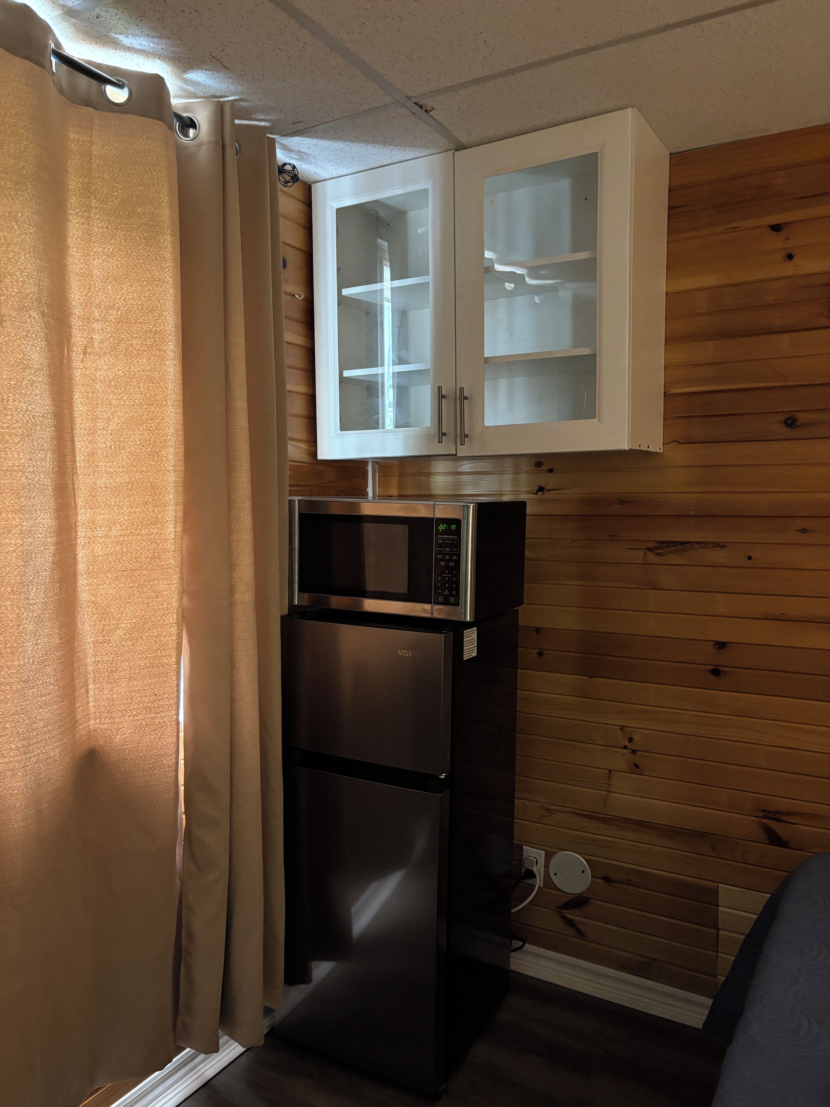A compact kitchen with a microwave, refrigerator, and wooden wall cabinets.