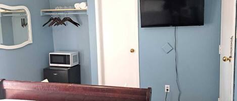 A bedroom with a bed, a television mounted on the wall, a door, and a ceiling fan.