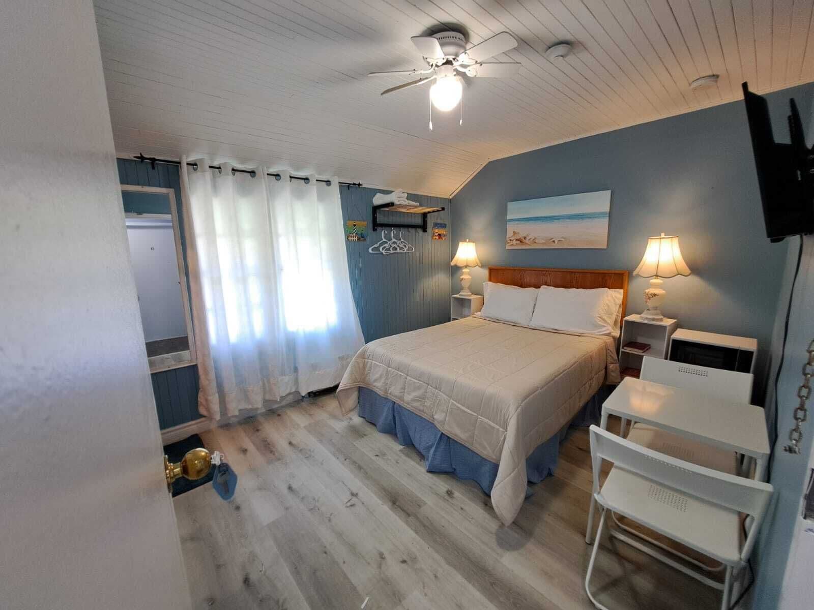 A bedroom with a bed, two bedside lamps, a ceiling fan, a TV, and a small table.