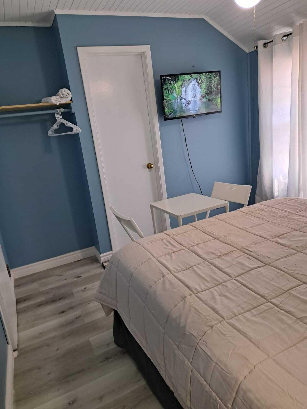 A bedroom with a bed, a TV mounted on the wall, a small table, and a chair.