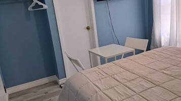 A bedroom with a bed, a TV mounted on the wall, a small table, and a chair.
