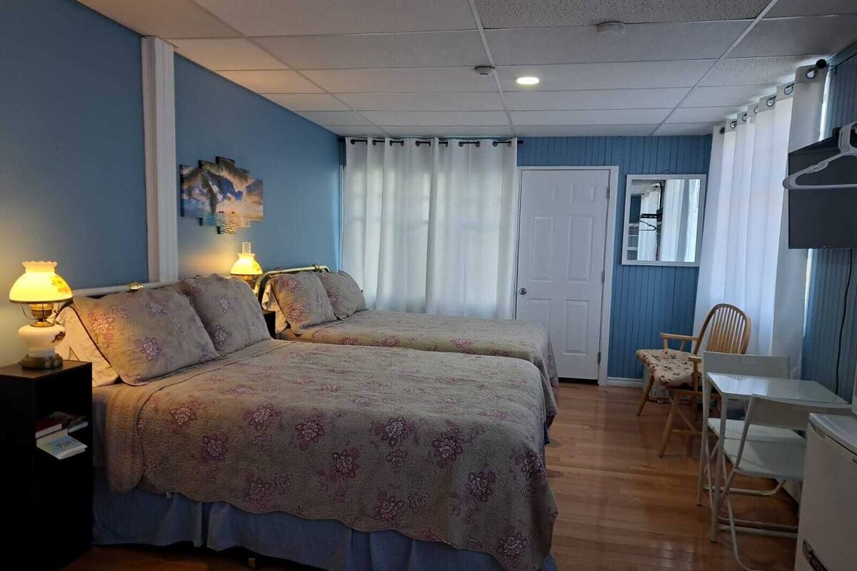 A hotel room with two beds, a desk, a chair, a TV, and a door.