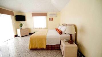 A bedroom with a bed, bedside table, lamp, dresser, TV, and a window.