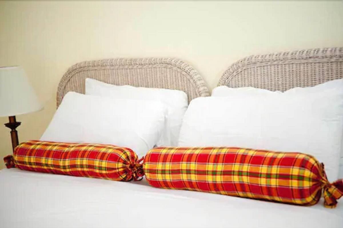 Un lit avec des oreillers blancs et un coussin à motifs écossais.