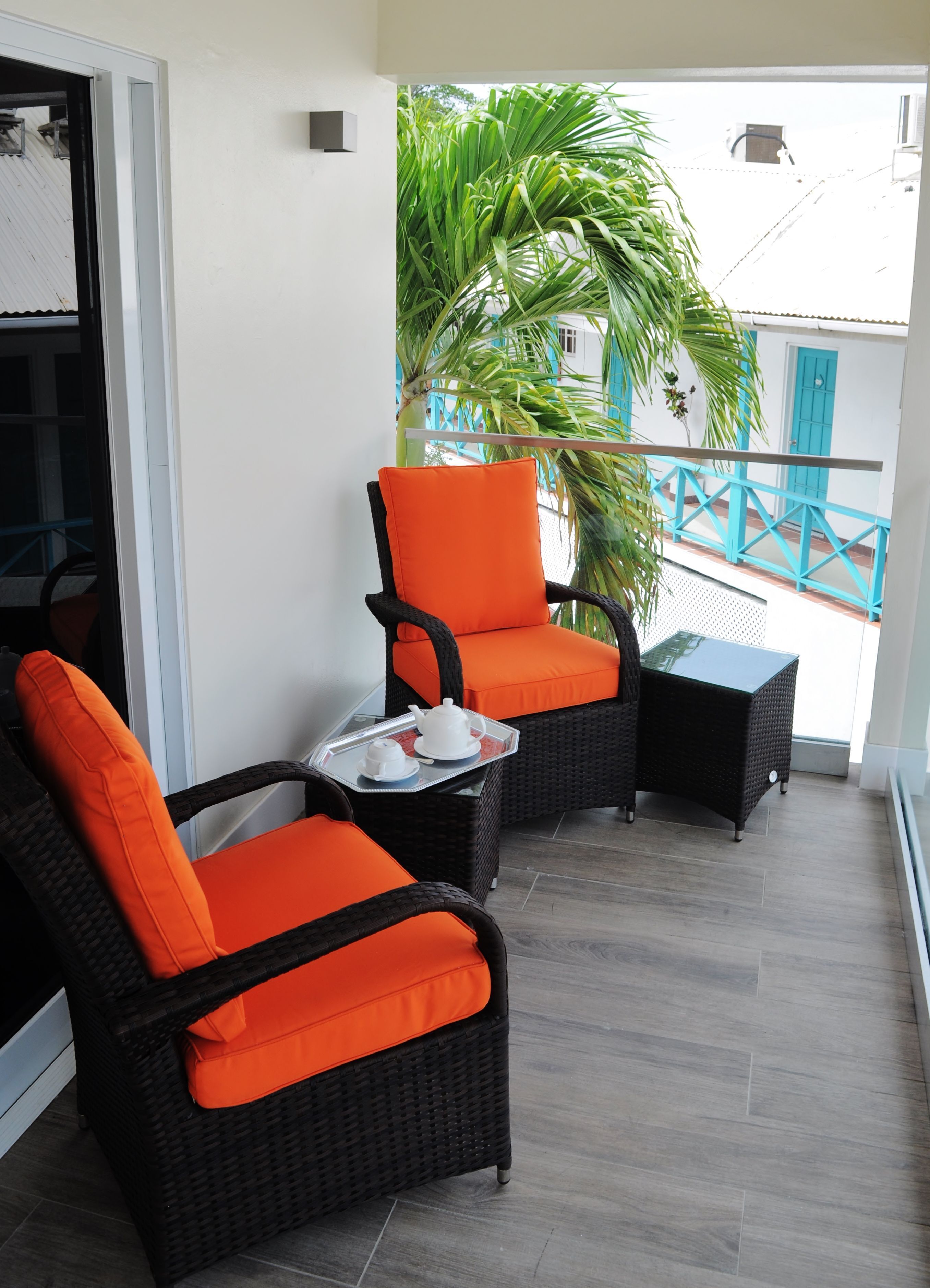 A balcony with wicker furniture, including two chairs and a small table, and a potted plant.