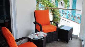 A balcony with wicker furniture, including two chairs and a small table, and a potted plant.