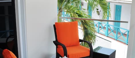 A balcony with wicker furniture, including two chairs and a small table, and a potted plant.