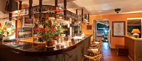 A bar area with a curved counter, wooden chairs, and a variety of bottles and glasses.