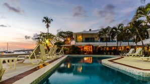 A swimming pool with lounge chairs and a building with a balcony in the background. - Mariners Hotel (Villa)