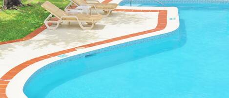 Una piscina con borde de azulejos, sillas de descanso y un borde de ladrillo.