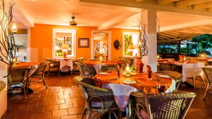 A restaurant with wicker furniture, orange walls, and a tiled floor. - Mariners Hotel (Villa)