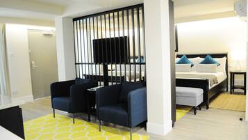 A modern hotel room with a bed, two armchairs, a TV, and a yellow patterned rug.