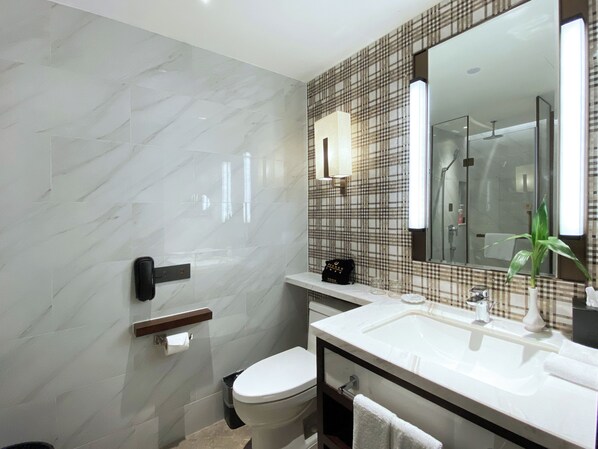 Un baño moderno con pared de mármol, inodoro, lavabo con espejo y zona de ducha.