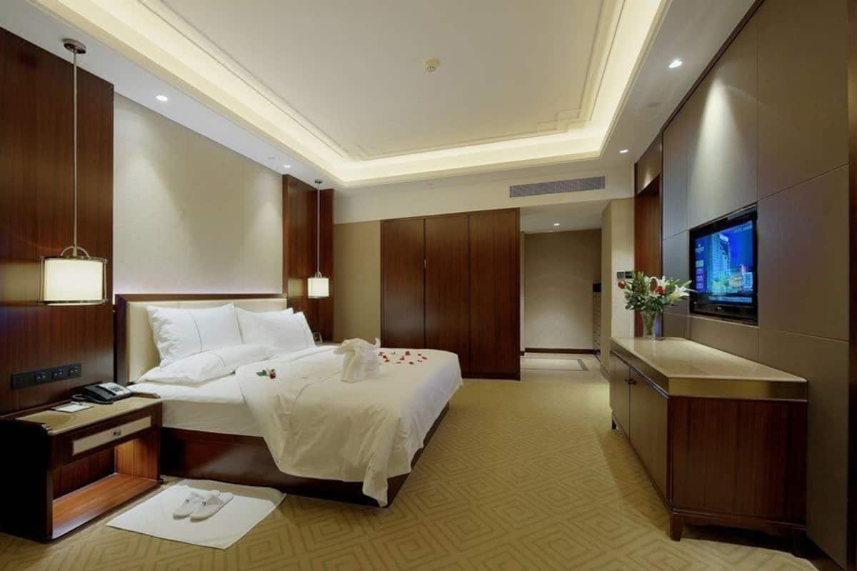Een hotelkamer met een groot bed, een nachtkastje met een lamp, een televisie aan de muur en een houten garderobe.