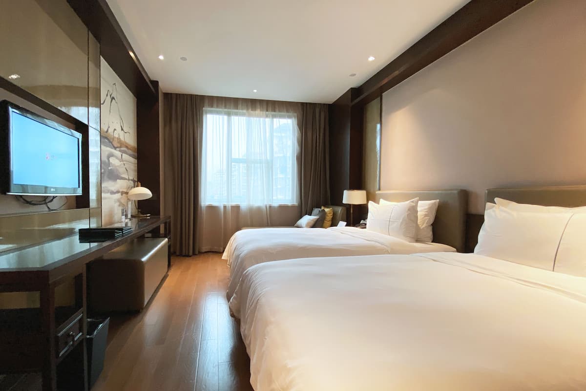 Een hotelkamer met een groot bed, een televisie op een bureau en een raam met gordijnen.