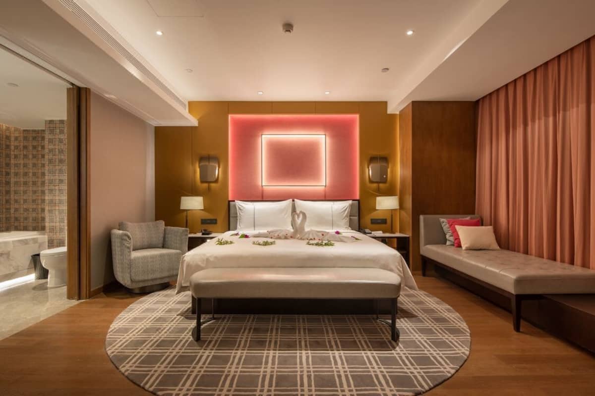 Een moderne hotelkamer met een groot bed, een bank, een fauteuil en een zichtbare badkamer door een glazen deur.