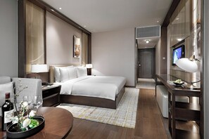 A modern hotel room with a bed, bedside tables, a desk, and a television.
