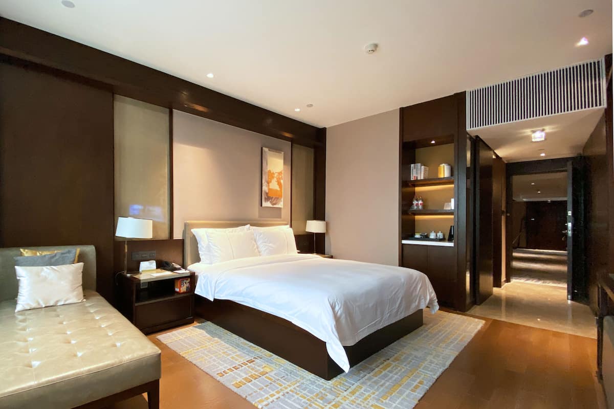 Een moderne hotelkamer met een groot bed, een nachtkastje, een lamp en een zithoek met een bankje.