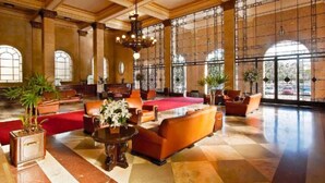 Un hall espacioso con alfombra roja, sofás de cuero, una mesa de centro y ventanas amplias.