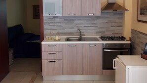 Una cocina compacta con muebles de madera clara, un lavamanos de acero inoxidable y una estufa a gas.