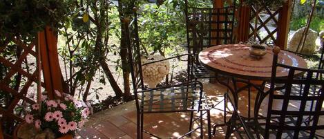 An outdoor patio with a round table and metal chairs, surrounded by potted plants and a wooden trellis.