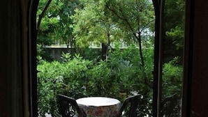 Vista a través de un arco de entrada a un patio exterior con una mesa y sillas redondas, rodeado de abundante follaje.