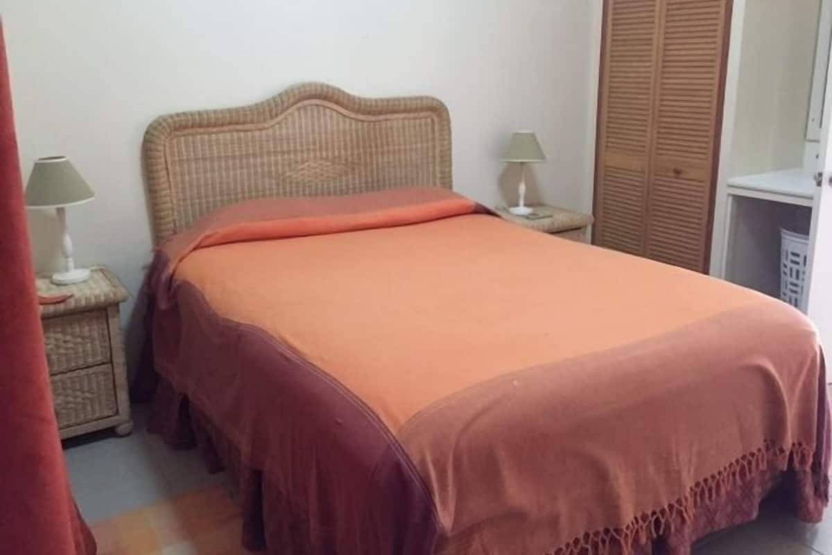 A bedroom with a single bed, a nightstand with a lamp, a wardrobe, and a small table with a lamp.