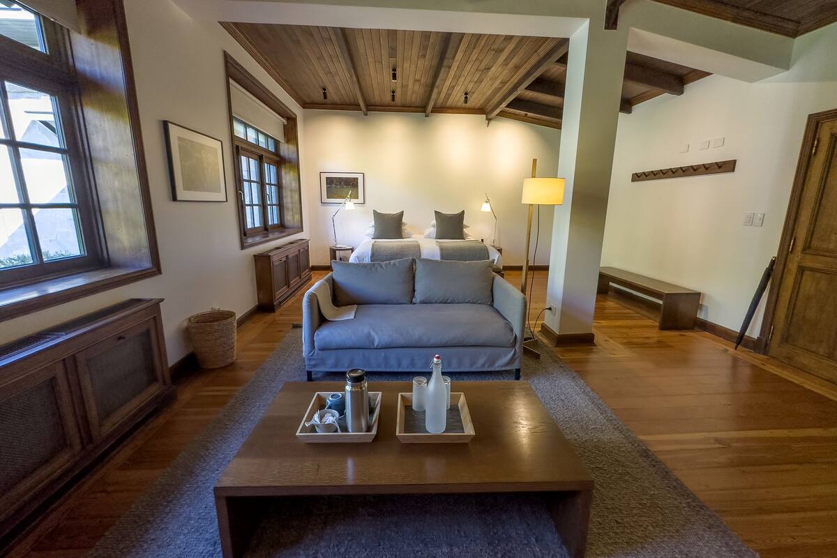 Una sala de estar acogedora con techo de madera, un sofá gris, una mesa de centro con dos bandejas y una lámpara.