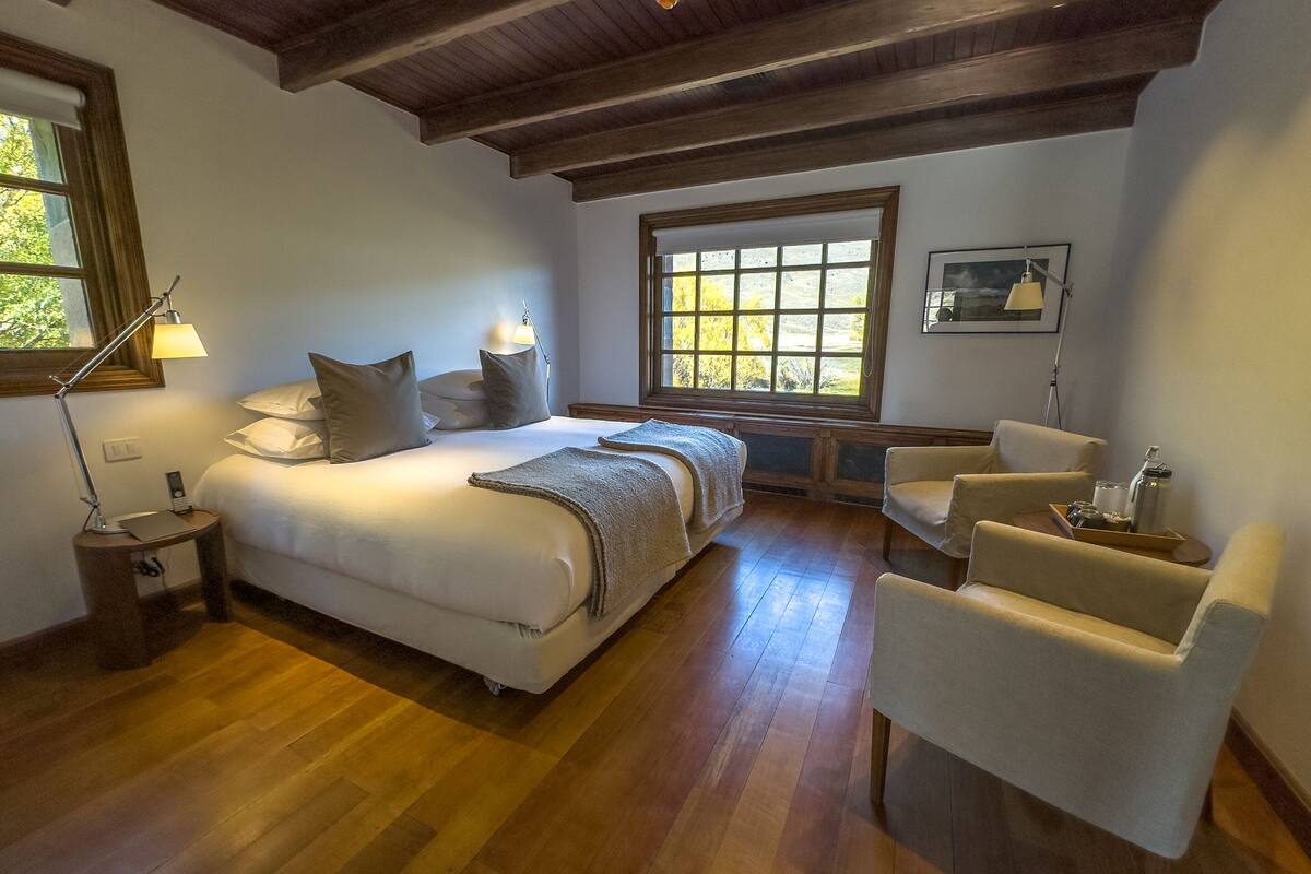 Un dormitorio con una cama grande, dos mesitas de noche, una silla y una ventana con vistas a árboles.