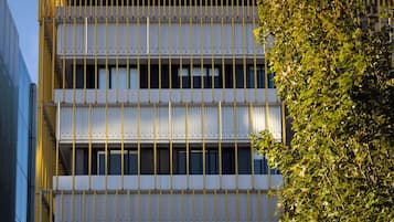A multi-story building with a grid-like facade, large windows, and a tree in the foreground.