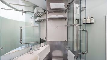 Un baño pequeño con mampara de vidrio, un lavamanos blanco, un espejo y una zona de ducha con puerta de vidrio.