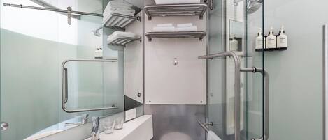 A compact bathroom with a glass partition, a white sink, a mirror, and a shower area with a glass door.