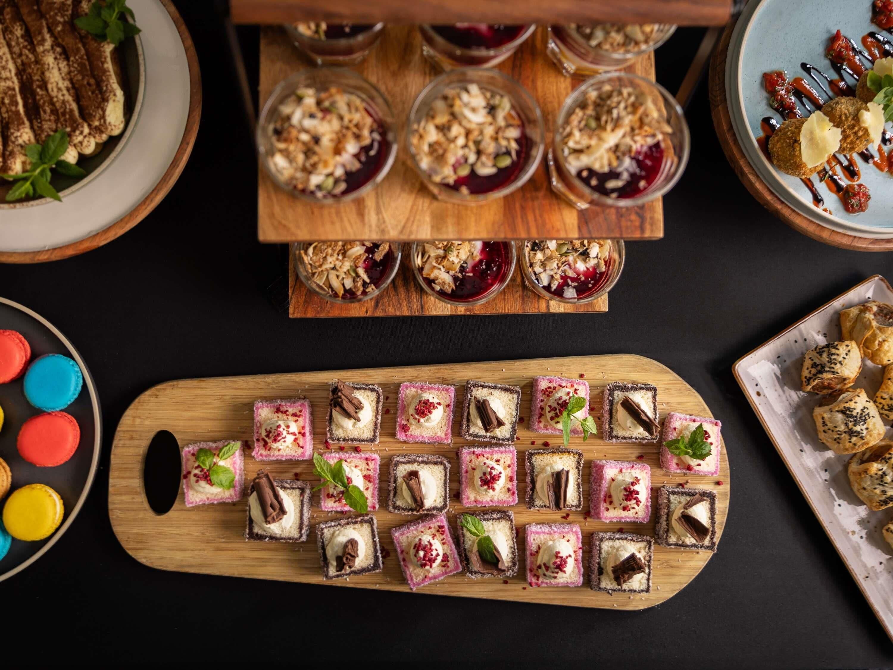 Una variedad de postres sobre una tabla de madera, incluyendo macarons, una bandeja de pasteles pequeños y un plato de pastelería.