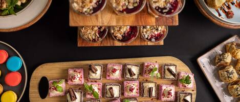 Une variété de desserts présentés sur une planche en bois, notamment des macarons, une barquette de petits gâteaux et une assiette de viennoiseries.