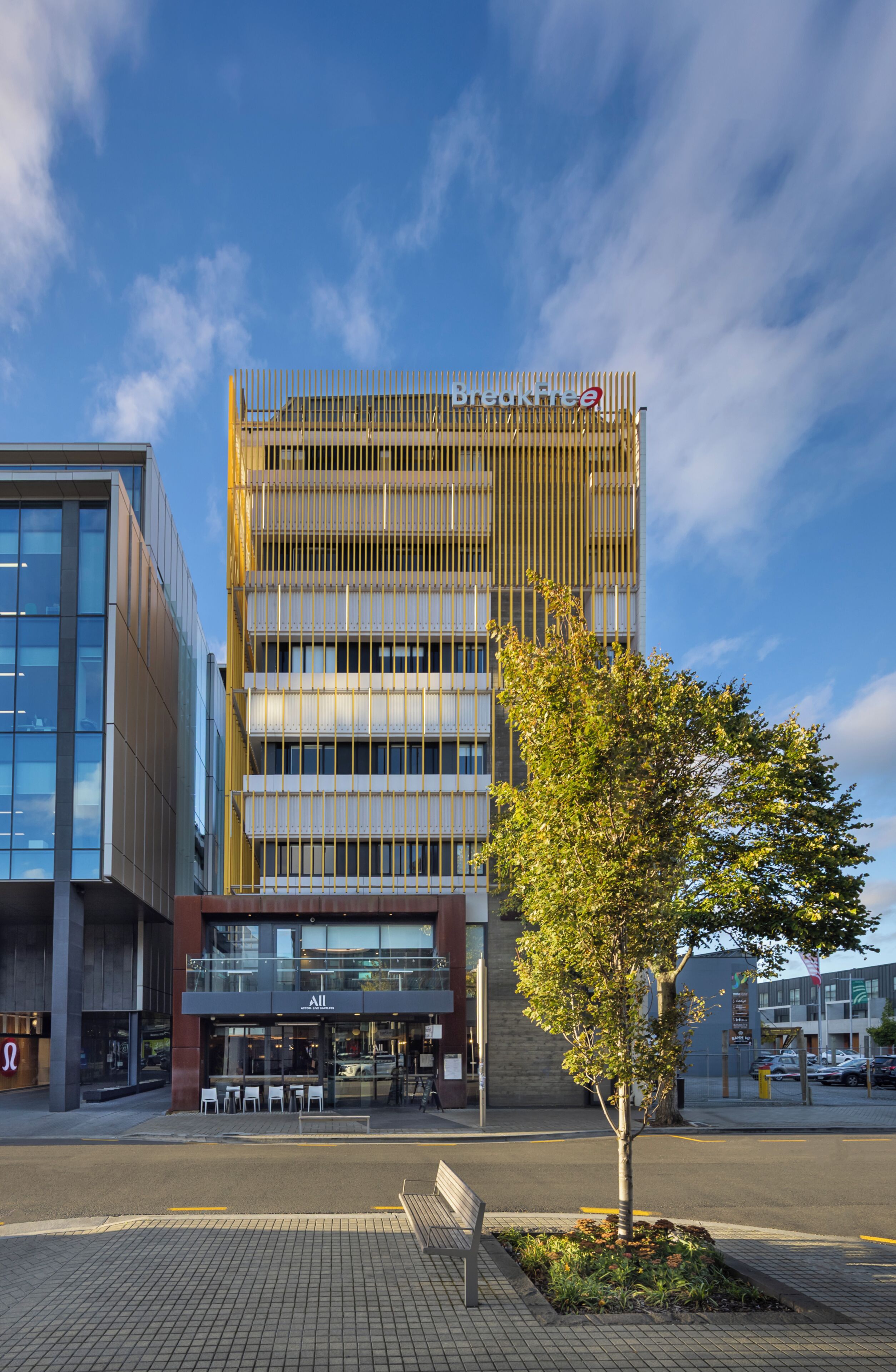 A modern building with a glass facade, a wooden fence, and a tree in front.