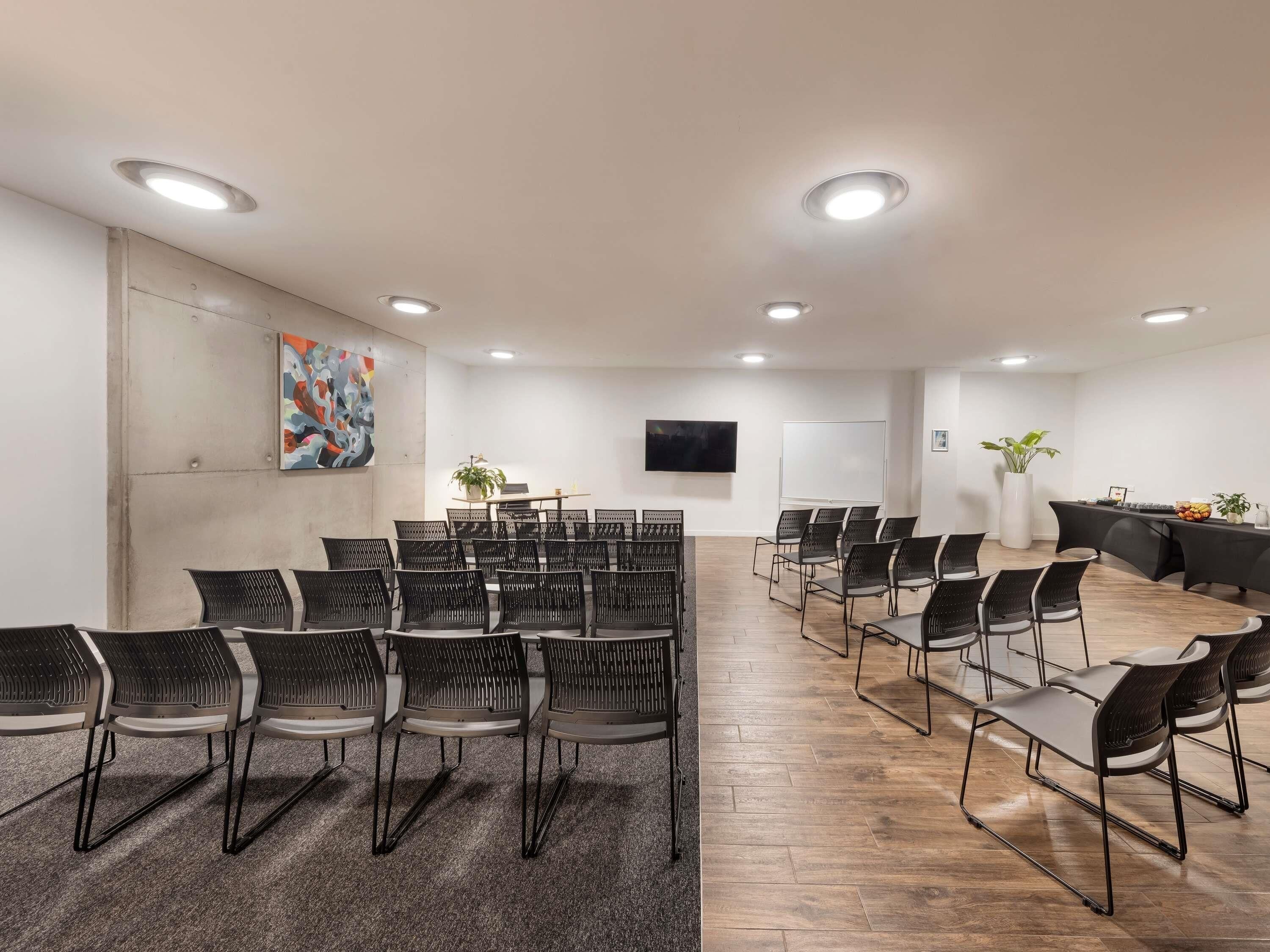 A conference room with black chairs, a whiteboard, a TV, and a plant.