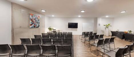 A conference room with black chairs, a whiteboard, a TV, and a plant.