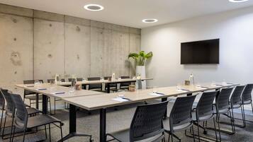 A conference room with a long table, chairs, a plant, a TV, and a concrete wall.