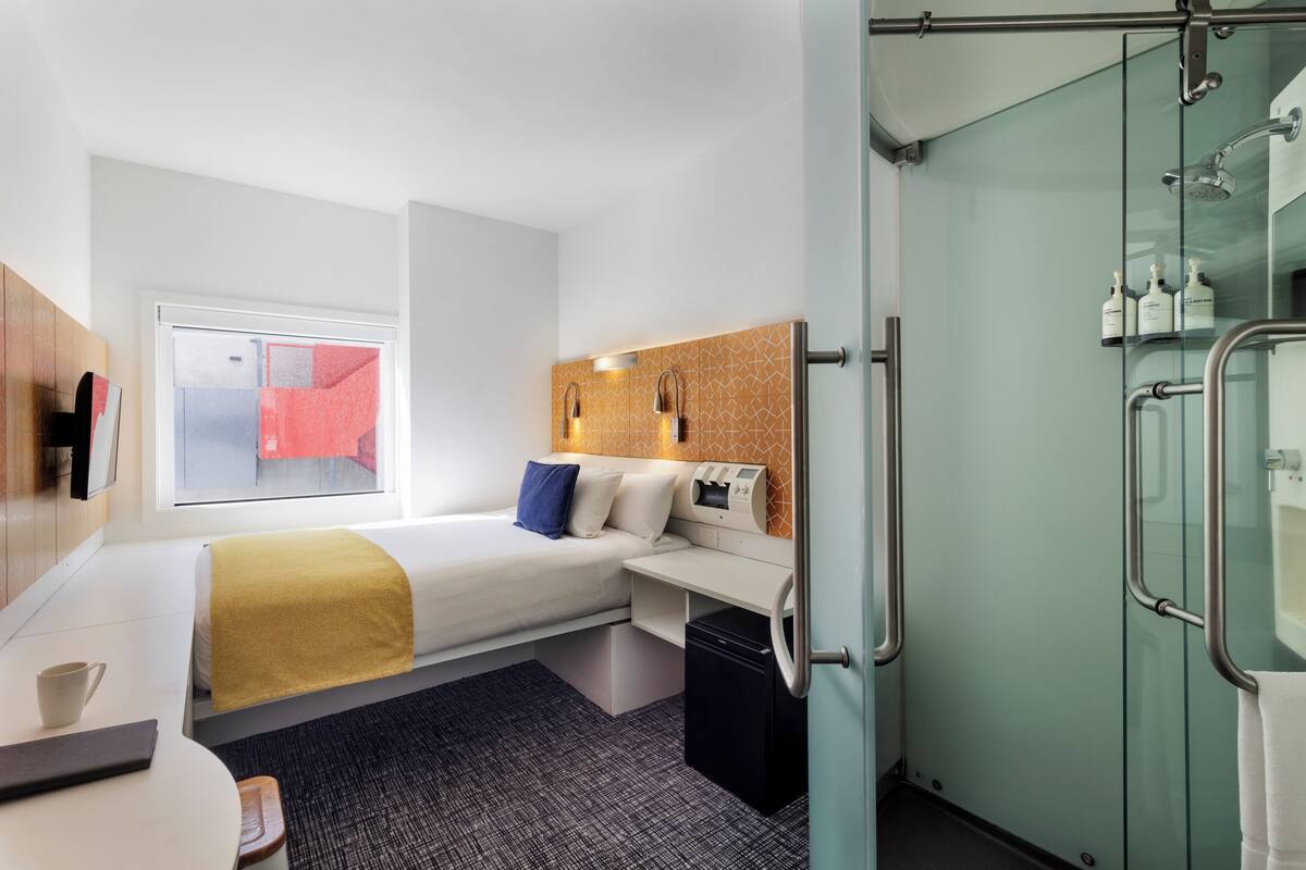 Habitación de hotel pequeña con cama, mesita de noche y un escritorio con silla.